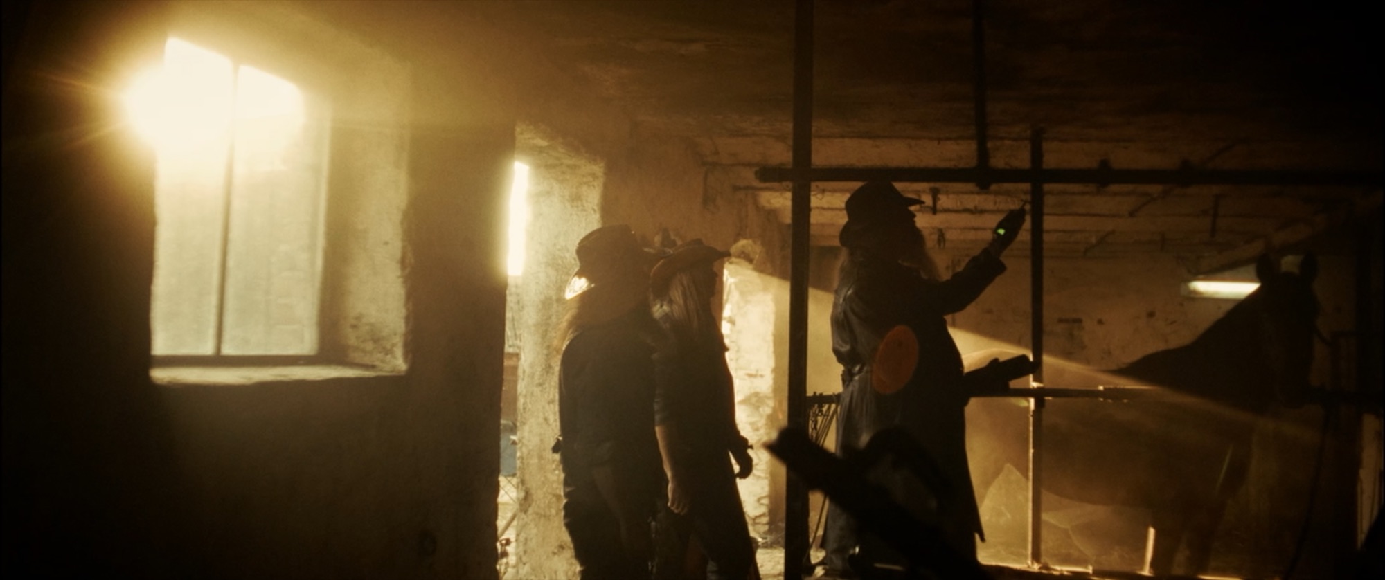 Silhouetted cowboys with a horse in a dusty barn, light streaming through a window - Amon Amarth